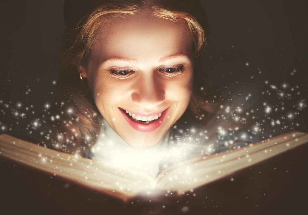 A woman joyfully discovers magic from an illuminated book.